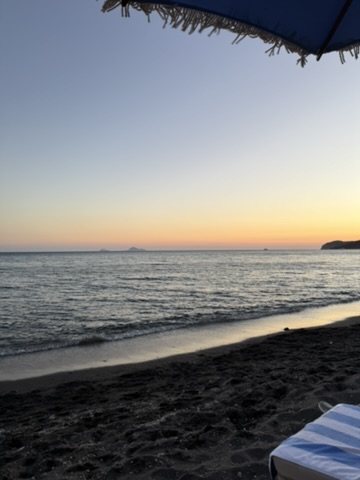 Dusk over a dark-sand beach, seen from under a beach umbrella
