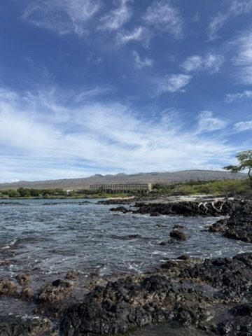Waves washing over black lava rock under a wide blue sky