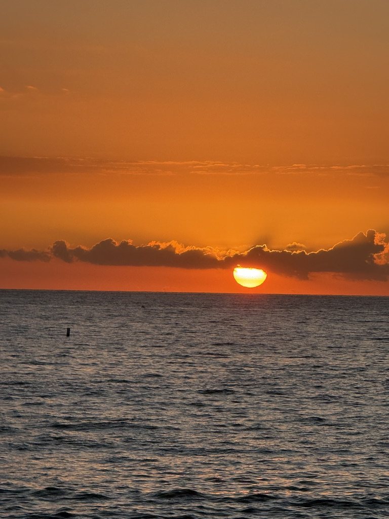 Orange sunset sinking into the ocean beneath a band of clouds